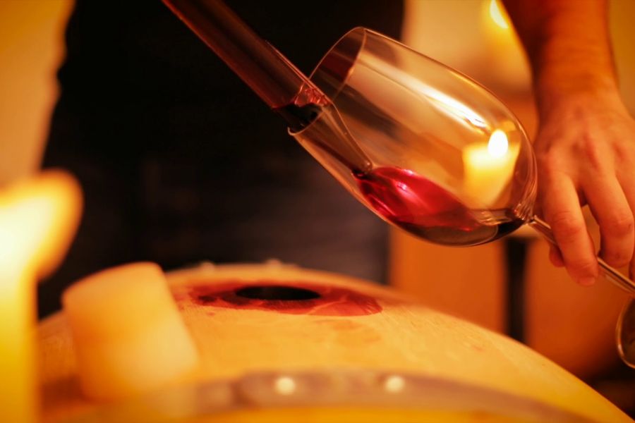 Rotwein läuft aus der Pipette ins Glas, Kerzen auf dem Fass