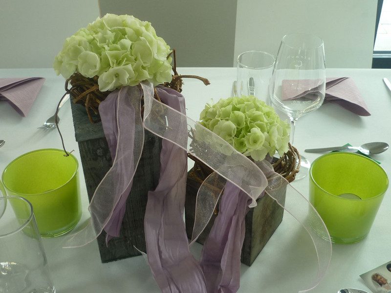 Gedeckter Tisch mit Blumenschmuck und grünen Gläsern